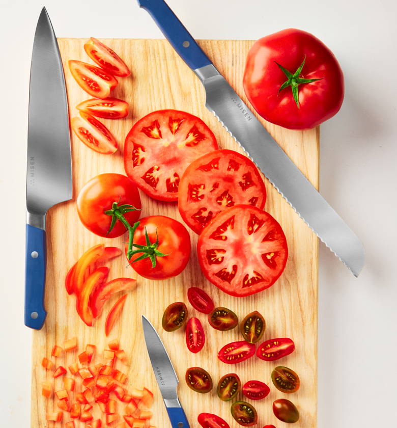 Misen chef knife, serrated bread knife, and paring knife with sliced tomatoes on cutting board