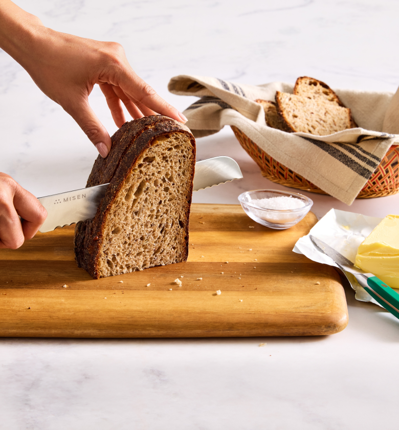 Misen serrated bread knife slicing sourdough loaf on wooden cutting board with butter and salt